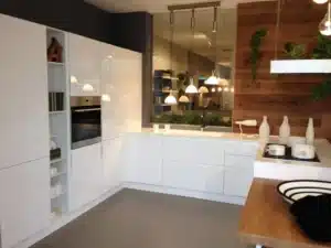 Cuisine moderne blanche et bois avec armoires laquées, four encastré, îlot central et plaques de cuisson. Mur d'accent en bois et plantes.