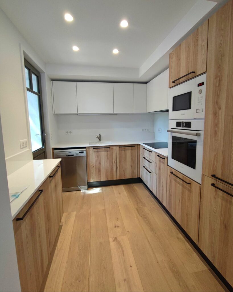 Cuisine moderne bois et blanc avec électroménager intégré Cuisine moderne en L avec meubles bas en bois clair, placards hauts blancs, plan de travail blanc et électroménager Bosch/Siemens intégré. Sol parquet.