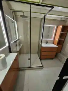 Salle de bain moderne avec douche à l'italienne vitrée, meuble-lavabo orange, miroir LED. Rangement mural assorti, carrelage clair.
