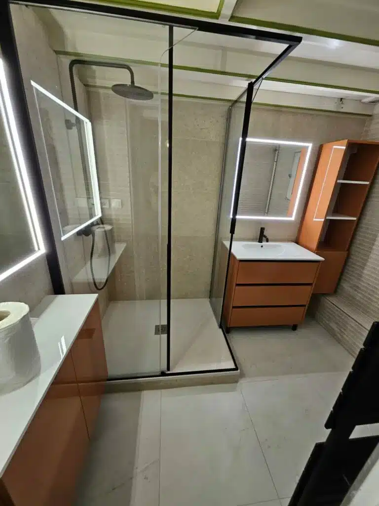 Salle de bain moderne avec douche à l'italienne vitrée, meuble-lavabo orange, miroir LED. Rangement mural assorti, carrelage clair.