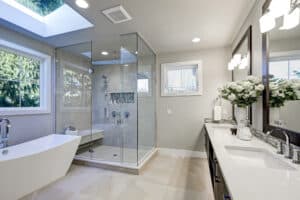 Salle de bain moderne lumineuse avec baignoire autoportante, douche vitrée carrelée, double vasque, grand miroir et puits de lumière.