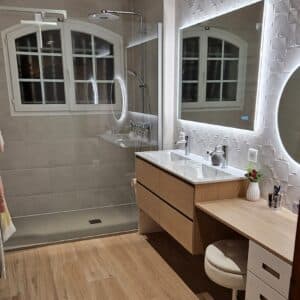 Salle de bain moderne avec douche à l'italienne, double vasque en bois clair, miroirs LED, et carrelage texturé. Fenêtre visible.